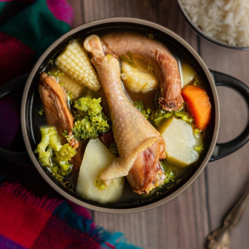 Peruvian chicken soup with corn, potatoes, carrots, and broccoli in a black bowl.