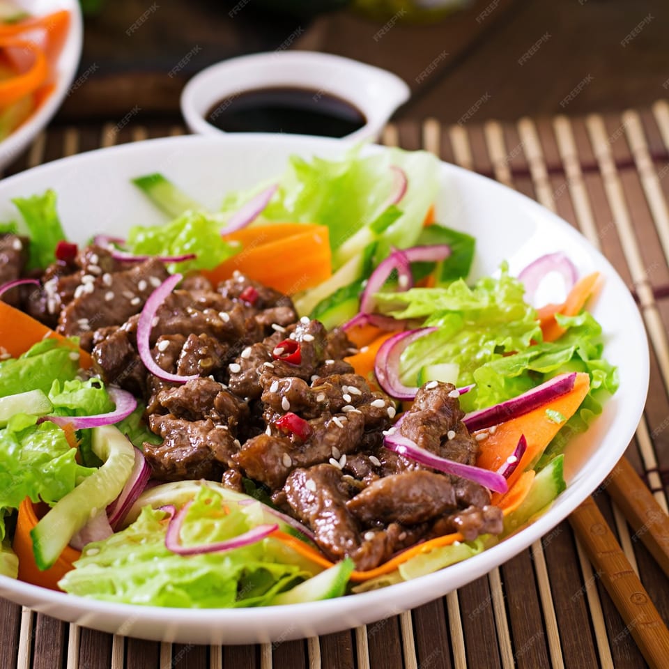 Peruvian Lomo Saltado salad with beef, lettuce, carrots, red onion, and cucumber in a white bowl.