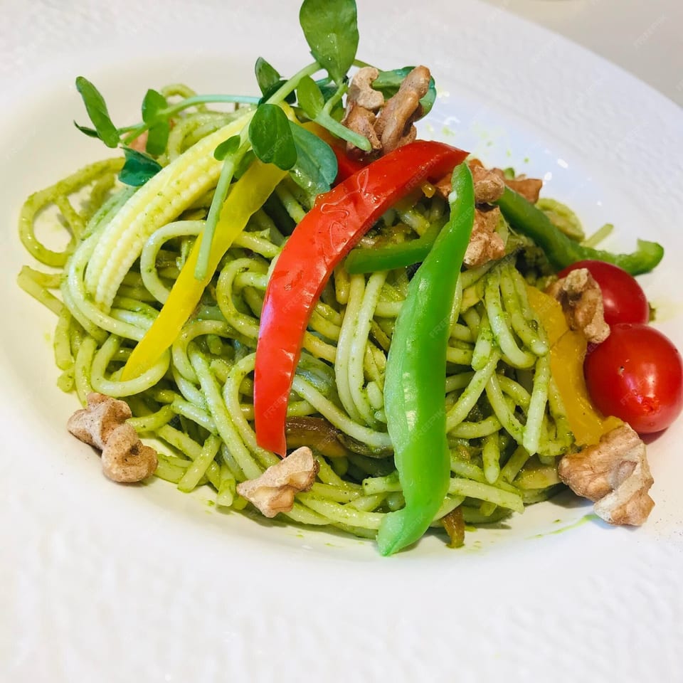 Peruvian pesto pasta with baby corn, bell peppers, cherry tomatoes, and walnuts on a white plate.