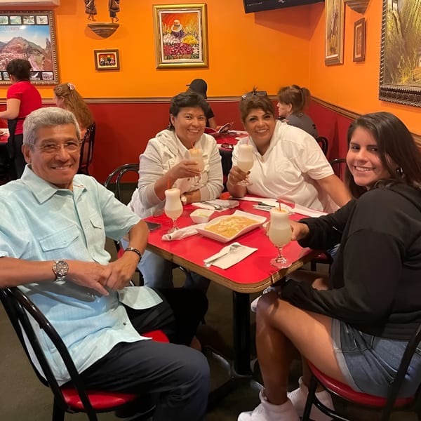 Four happy diners enjoying drinks and food at a red table in Con Sabor A Peru.