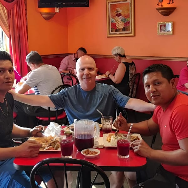 Three men smiling at a red table with Peruvian food and drinks at Con Sabor A Peru.